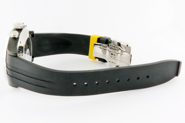 Side view of a black rubber watch strap with a stainless steel deployment clasp and a yellow spacer near the buckle.