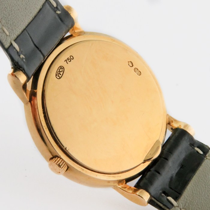 Gold wristwatch shown from the back, with a black leather strap and a crown at lower left; back case stamped 750 and decorative marks visible.