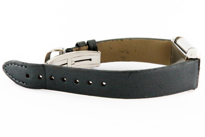 Black fabric watch strap with a silver deployment clasp laid flat beside the watch case.