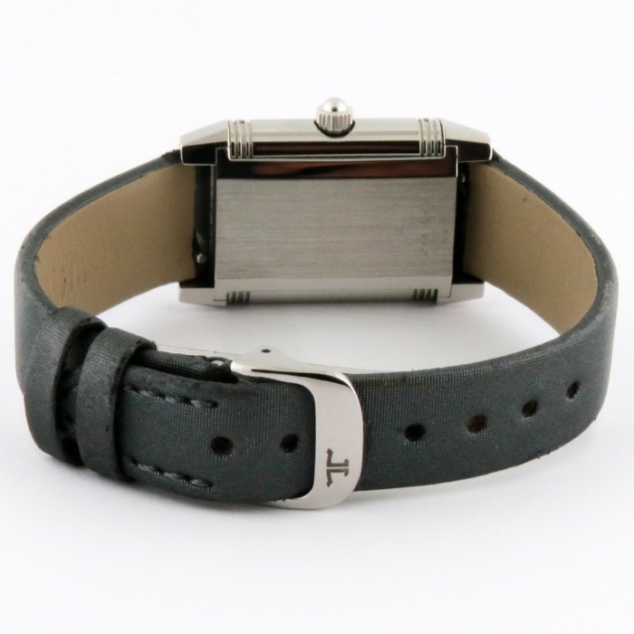 Close-up of a rectangular metal wristwatch laid on its side, showing a dark strap and a silver buckle with a small logo