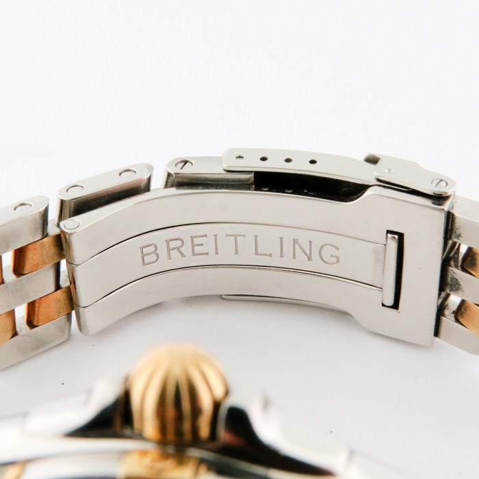 Close-up of a Breitling watch clasp in stainless steel with gold-accent bracelet links and engraved brand name.